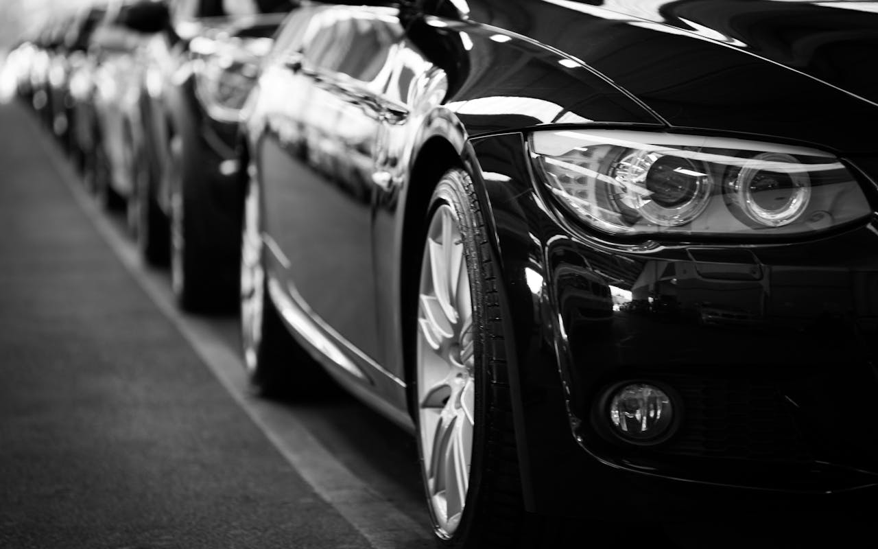 who-we-are Close-up black and white image of a luxury car line-up focusing on vehicle headlights.