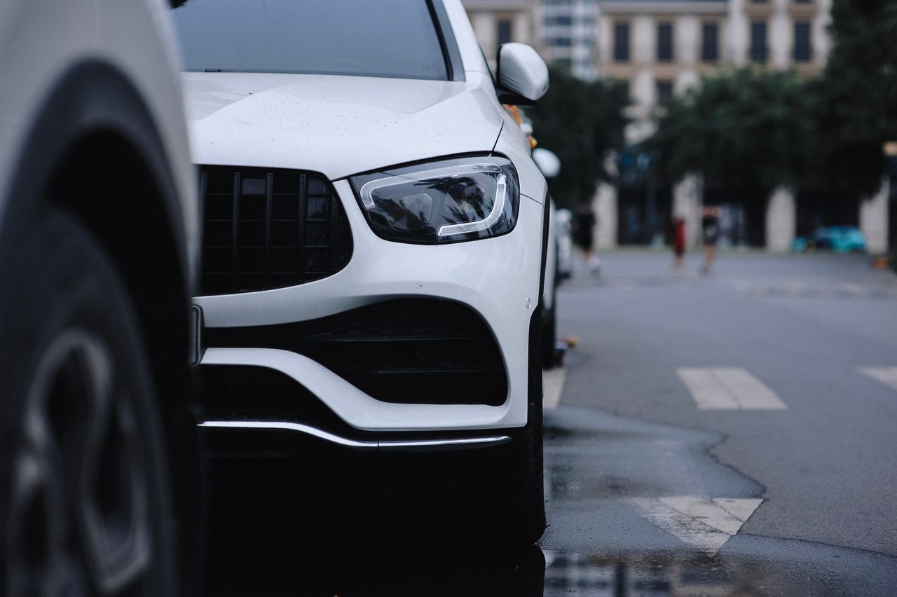 Close-up view of a sleek white car parked on a city street, reflecting urban style.